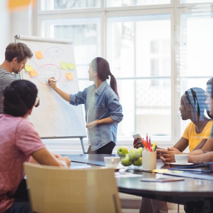 Business executives discussing with their colleagues on whiteboard during meeting at office